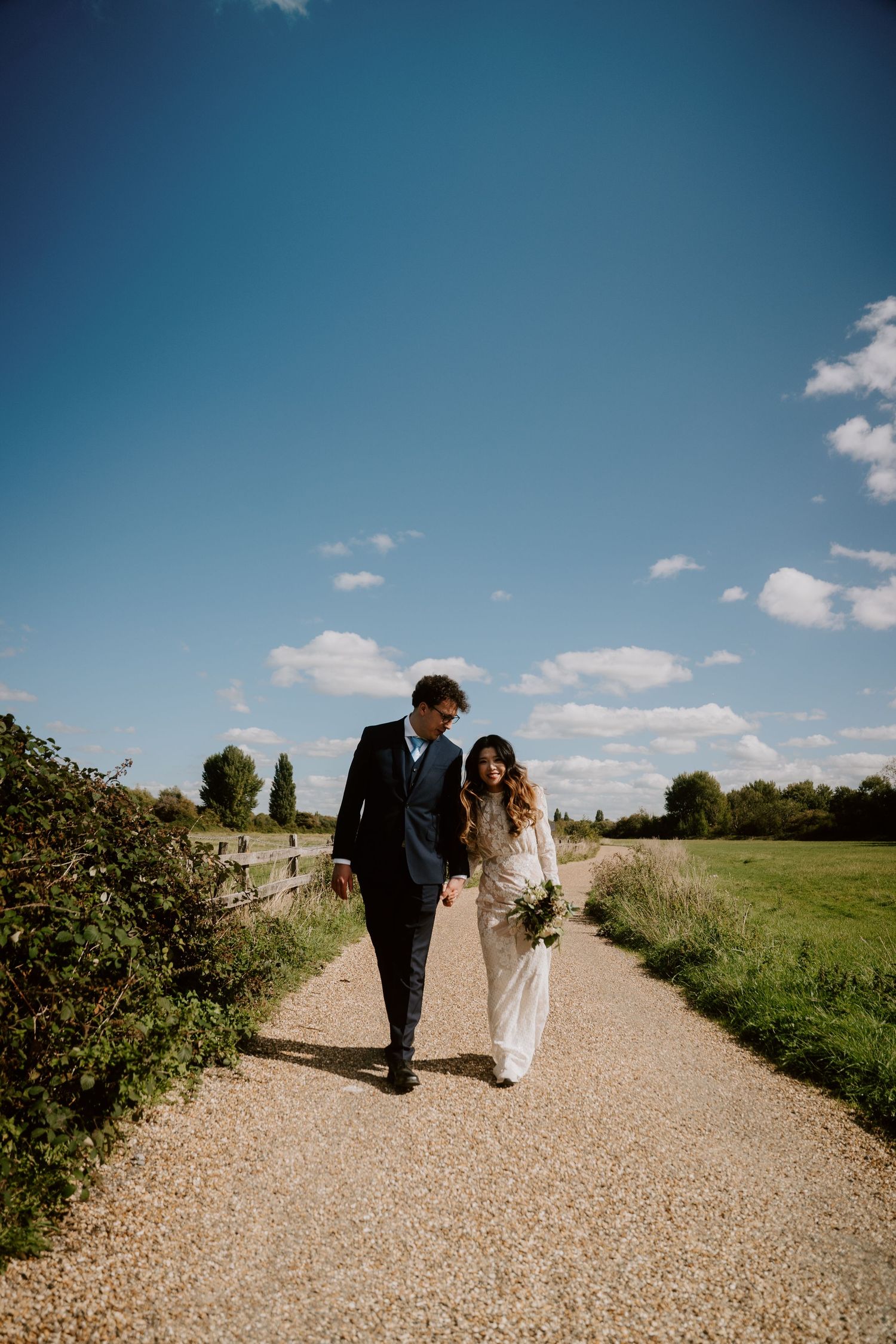 A couple walking along a gravel path on a sunny day with blue skies.
