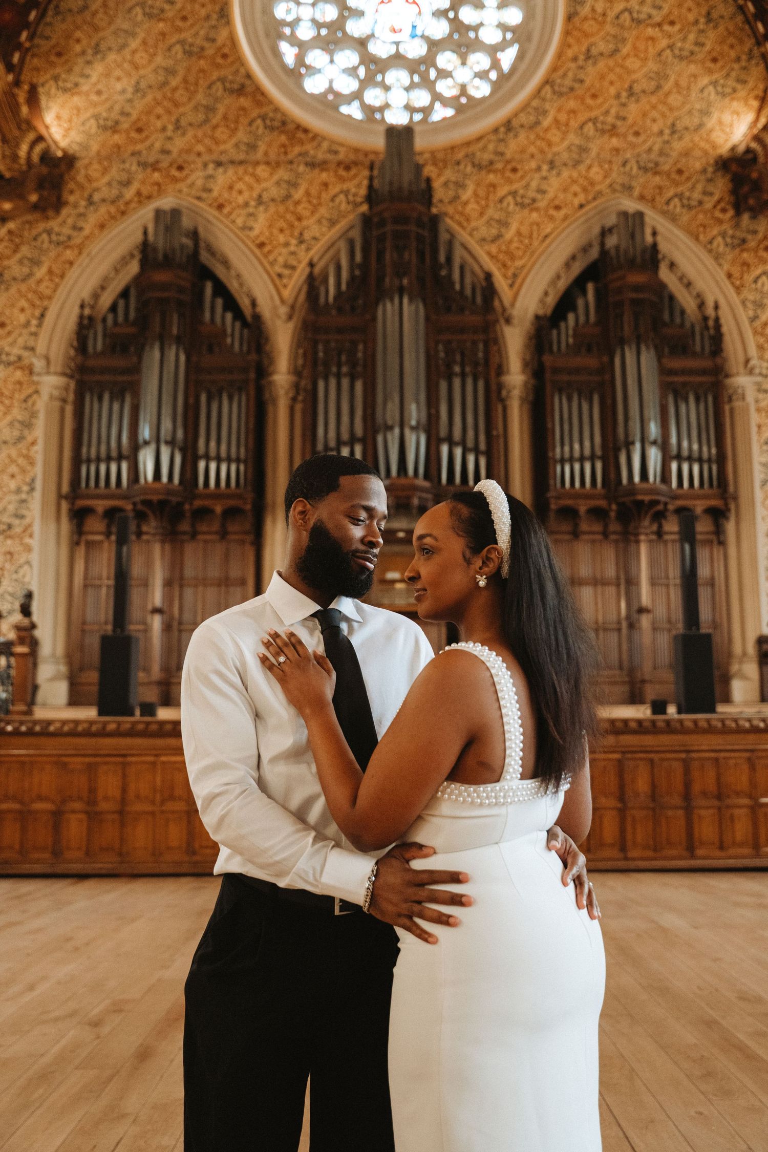 A couple in wedding attire embraces in an ornate chapel with a grand pipe organ and Gothic arched ceilings.