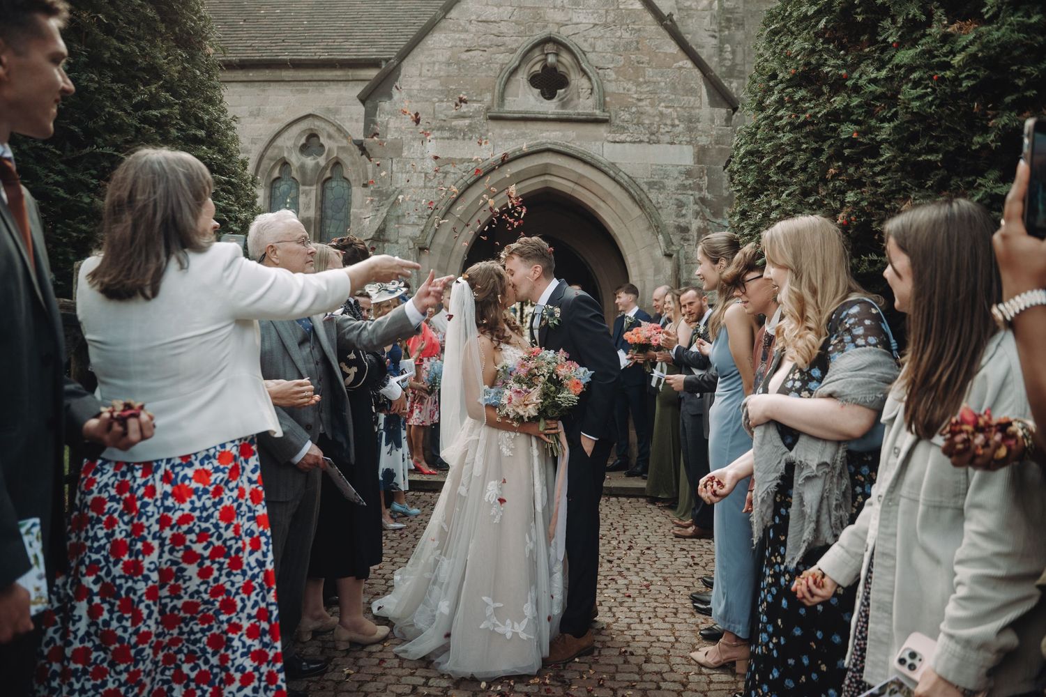 Wedding guests celebrating outside a historic stone church entrance.