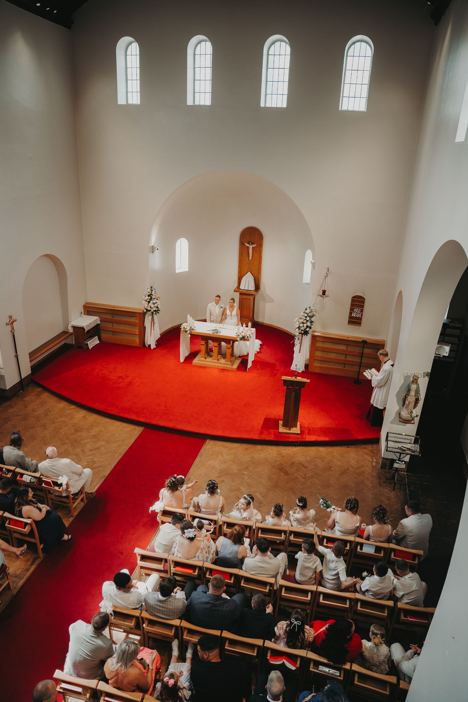Church sanctuary with red carpet and wooden pews during a wedding ceremony viewed from above.