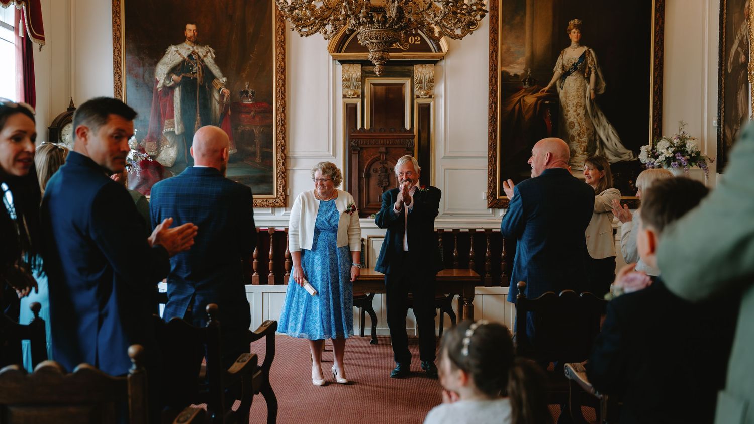 Wedding guests mingling in an ornate historic venue with gilded artwork.