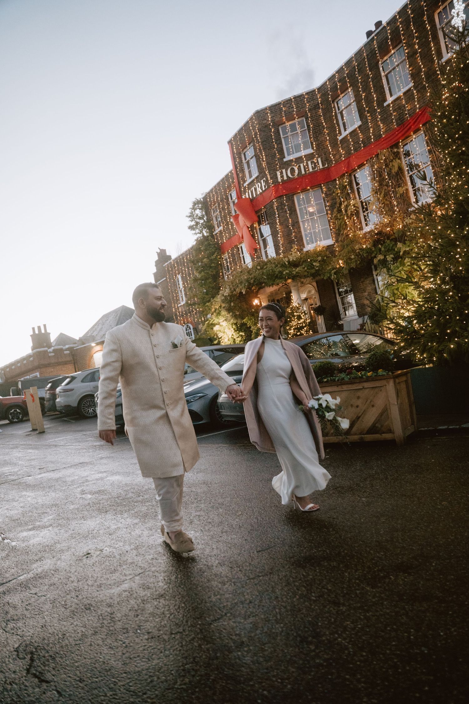 A couple runs playfully through a courtyard decorated with twinkling lights at dusk.
