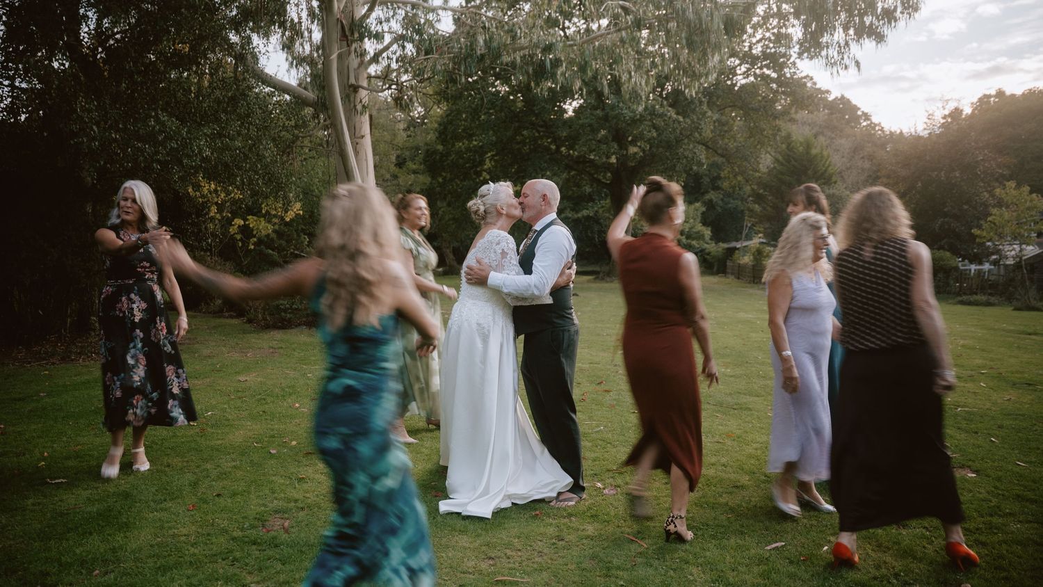 Wedding celebration with guests dancing outdoors at sunset.