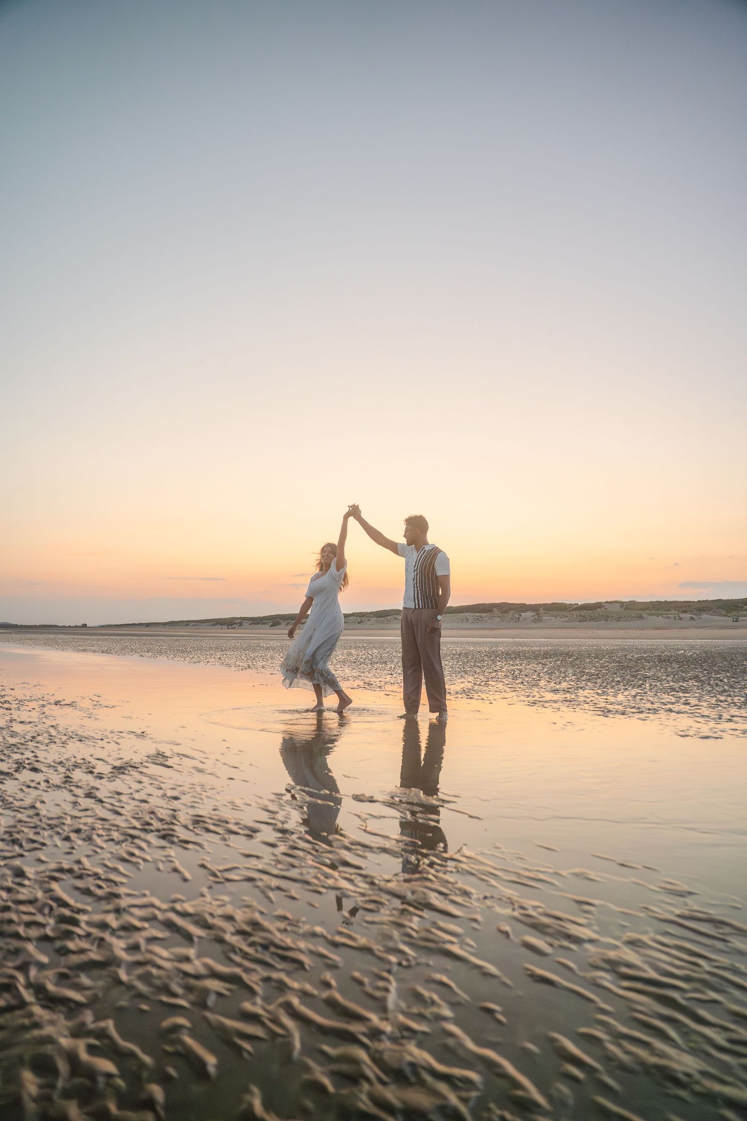 Silhouettes of couple dancing in shallow beach water during golden hour.
