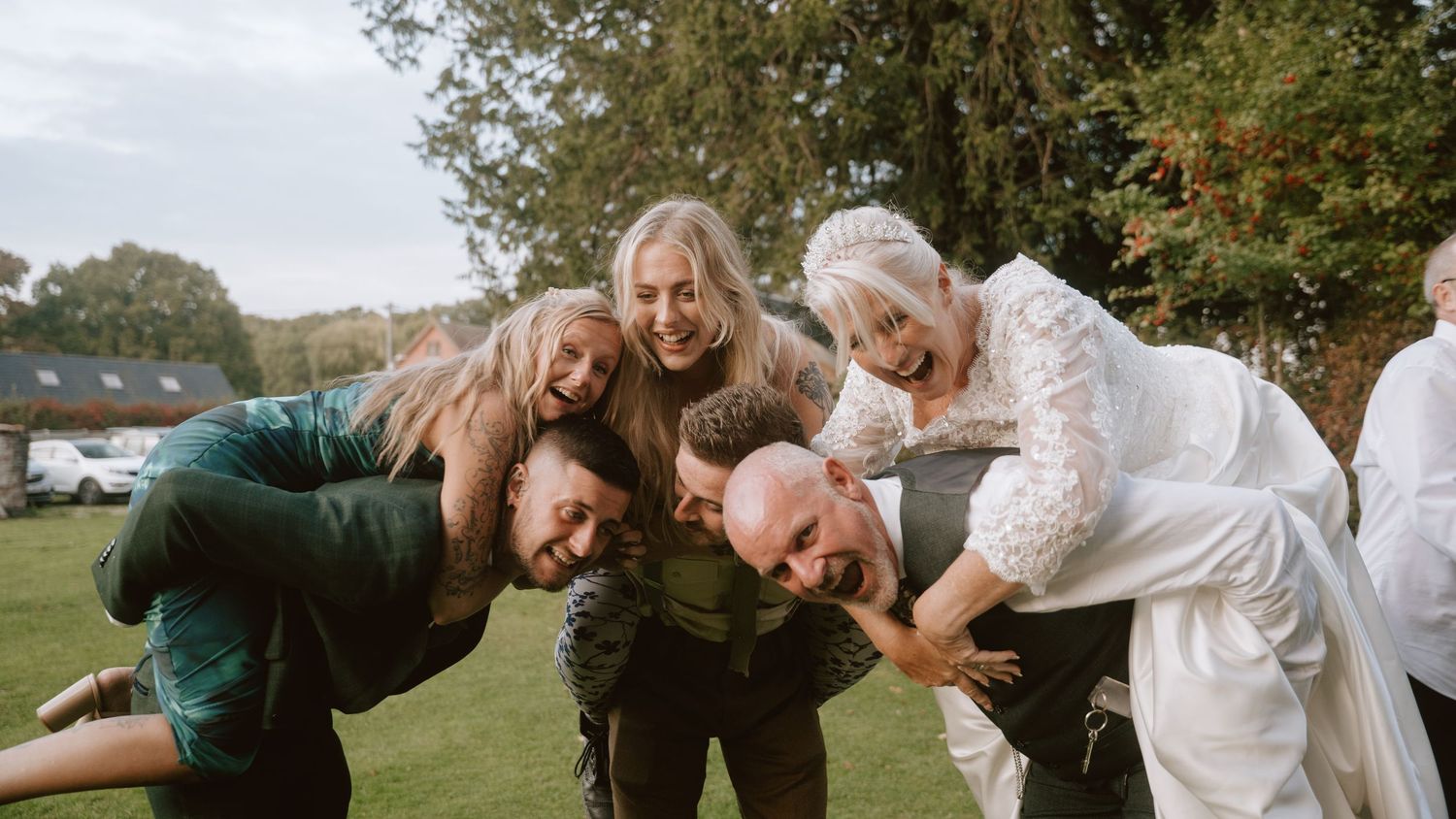 Wedding party members posing playfully outdoors in a group photo.