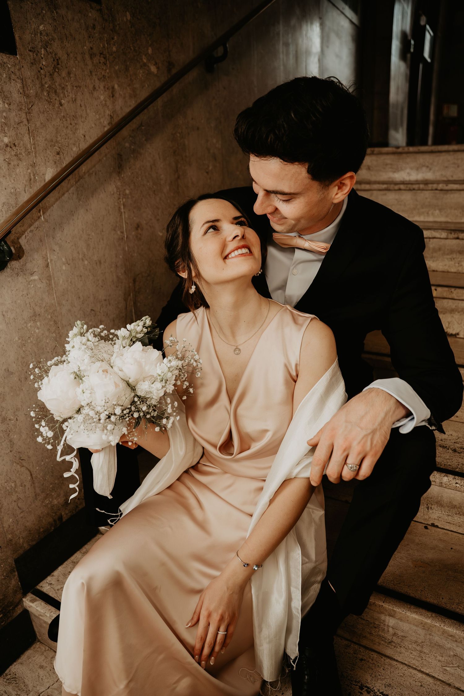 Romantic couple in formal attire sharing intimate moments on stone steps with white flowers.