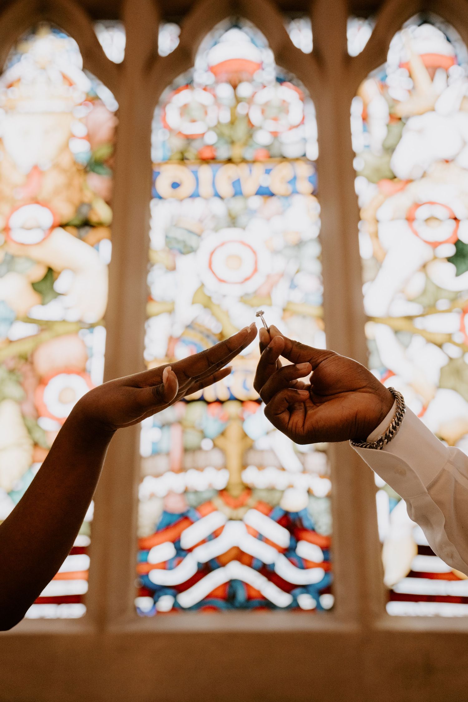 Silhouettes of hands performing a card trick against a colorful stained glass window background.