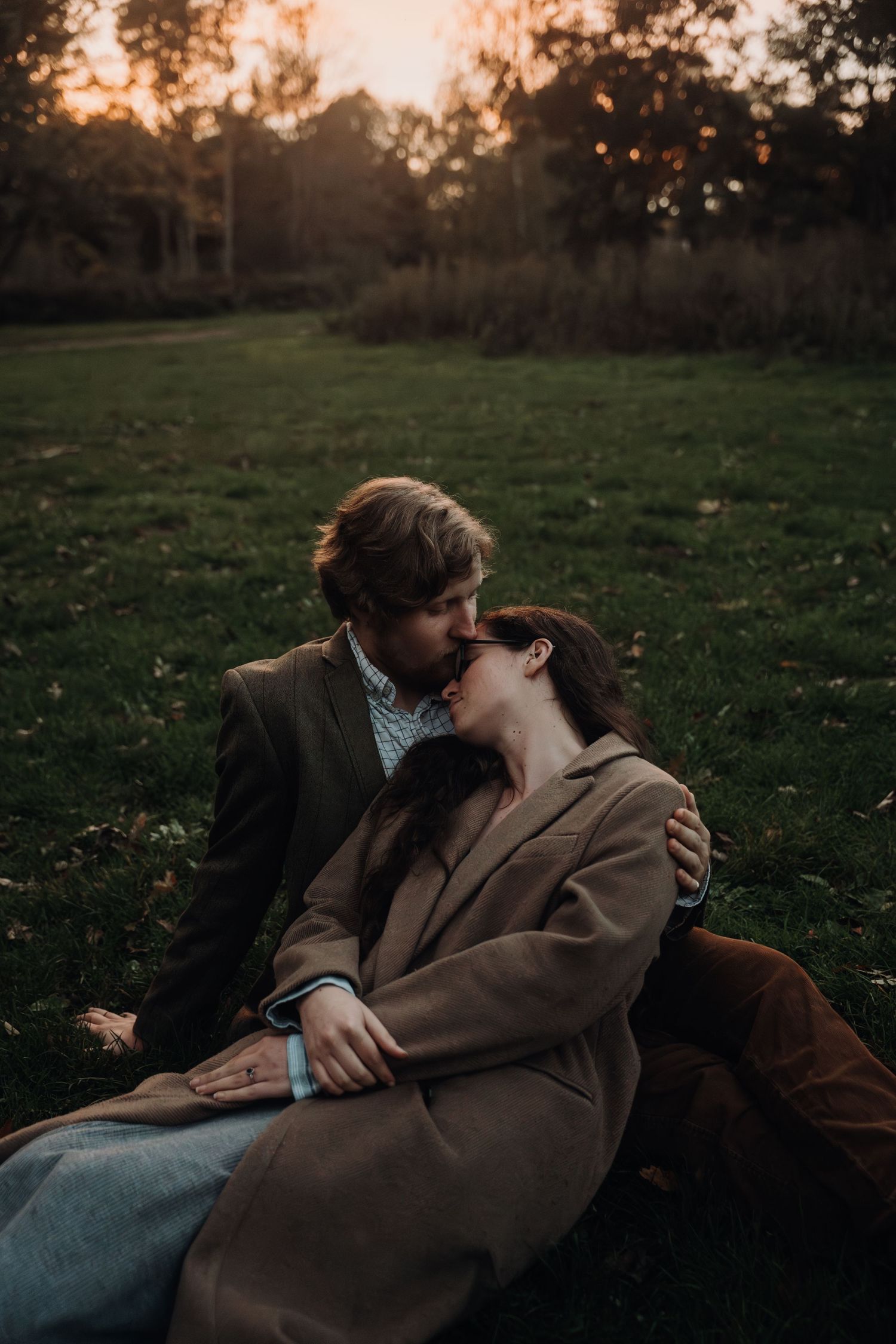 Couple embraces on blanket during romantic sunset photoshoot.