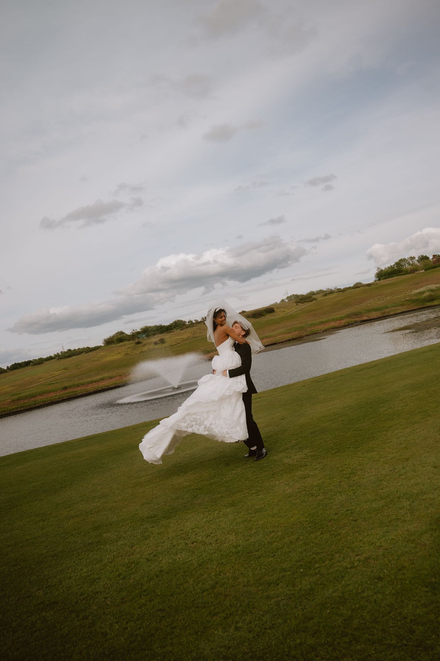 A bride and groom share a romantic spin on a lush green golf course with a scenic pond backdrop on their wedding day.