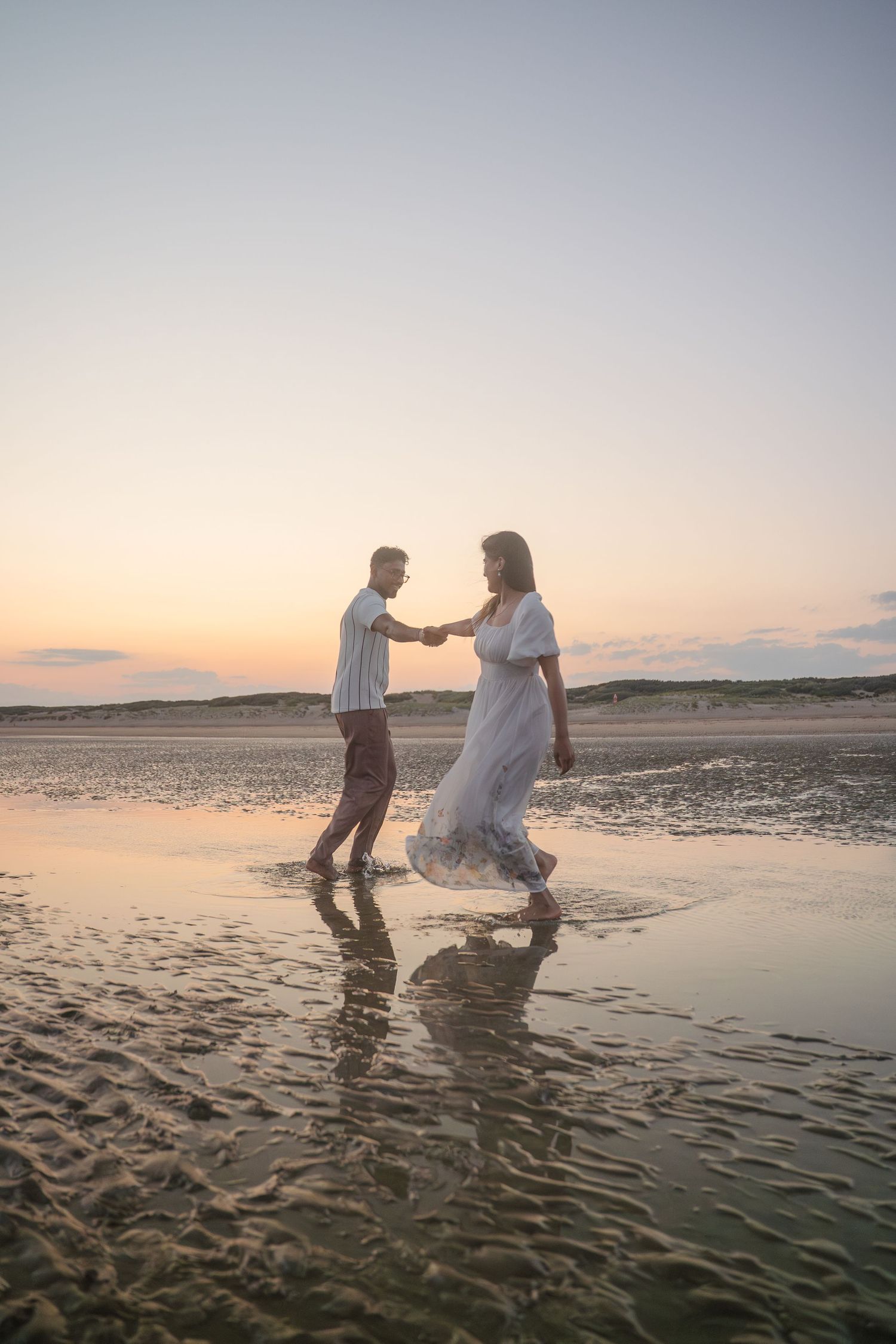 Couple dancing in shallow water at the beach during sunset.