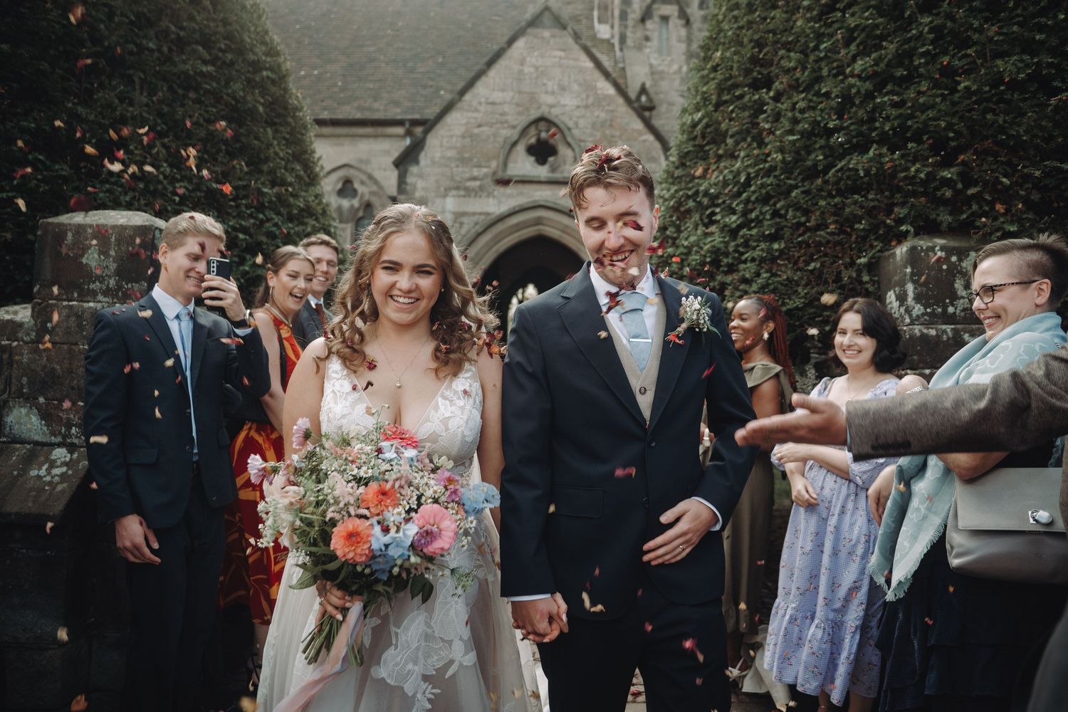 Wedding party celebrating with confetti outside a historic church building.