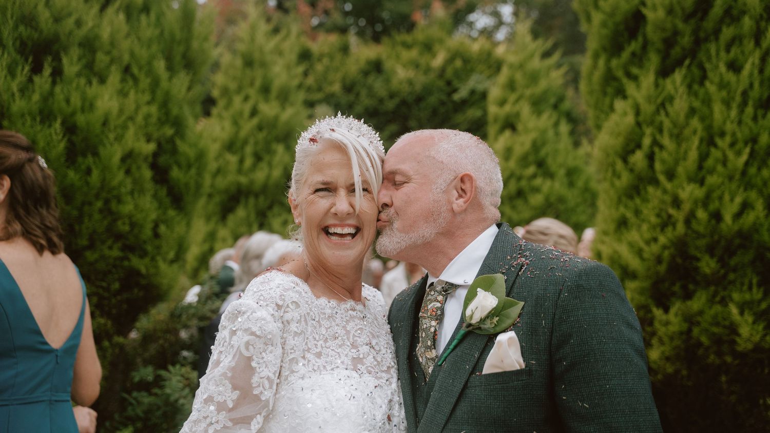Wedding celebration with guests and couple embracing in a garden setting.