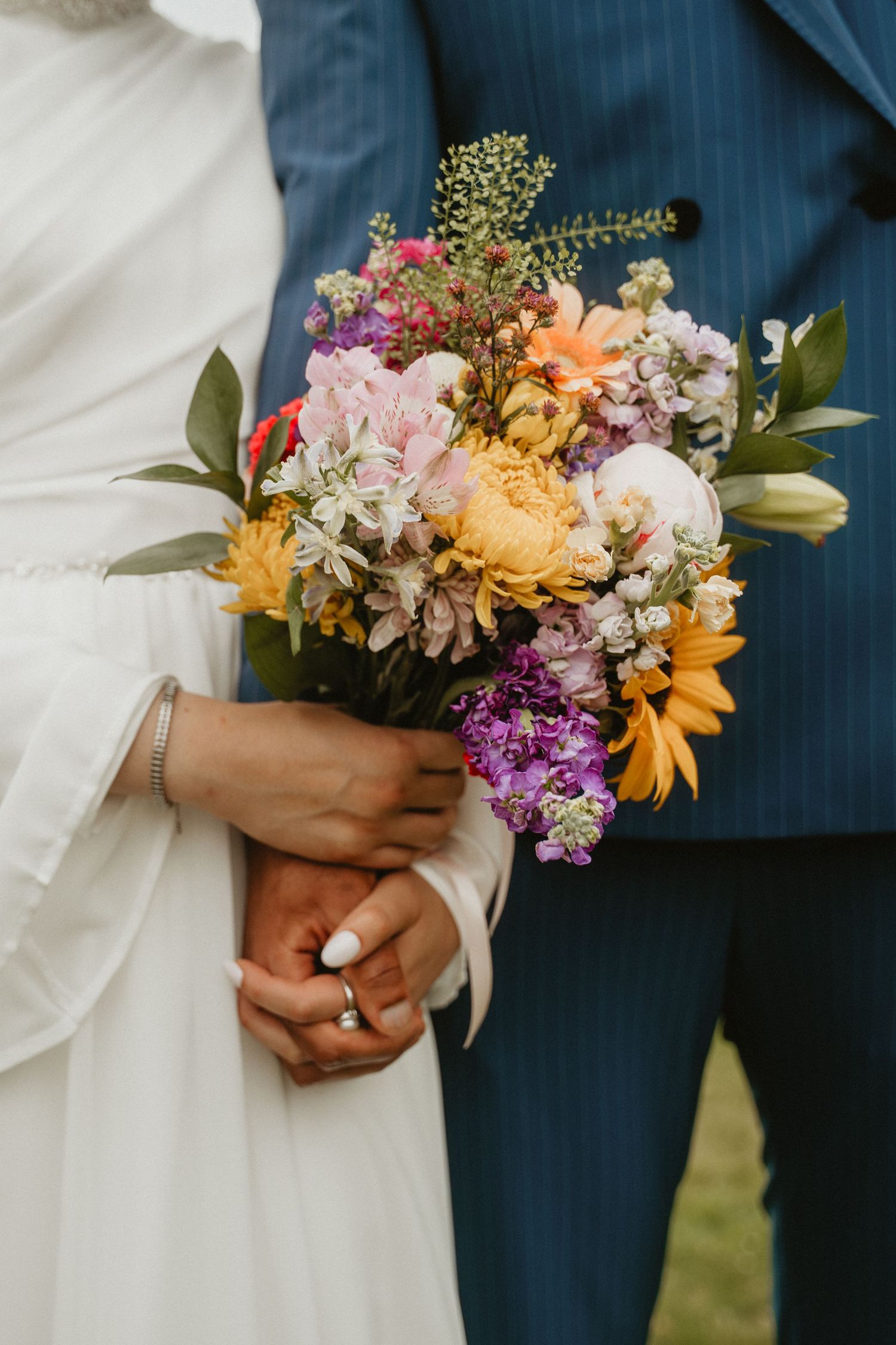 A colorful wedding bouquet with purple, orange and yellow flowers held against a navy blue suit.