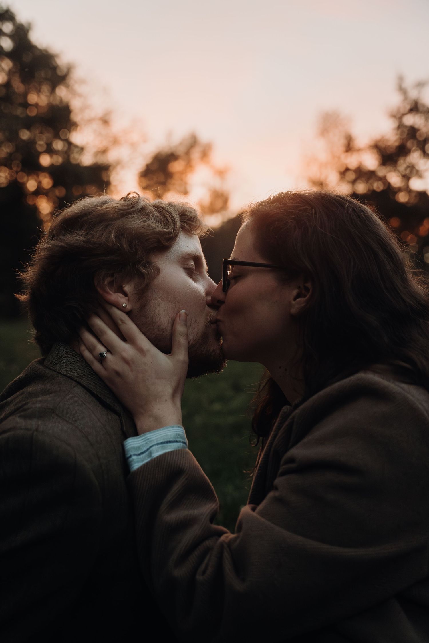Romantic couple sharing an intimate kiss at sunset with bokeh lighting in the background.