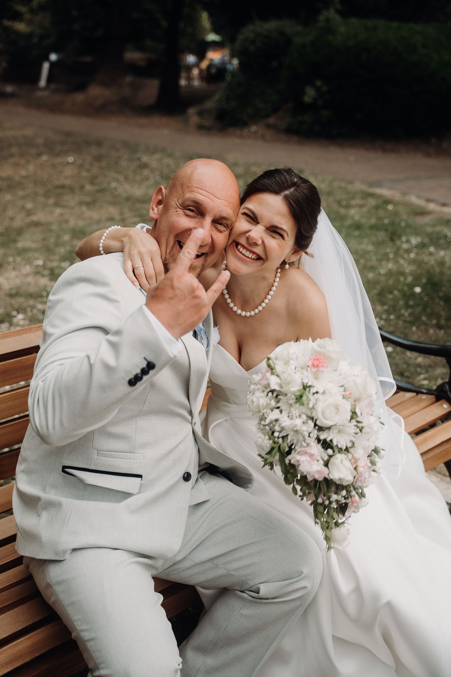 Tender wedding moment captured on a park bench with white floral bouquet.