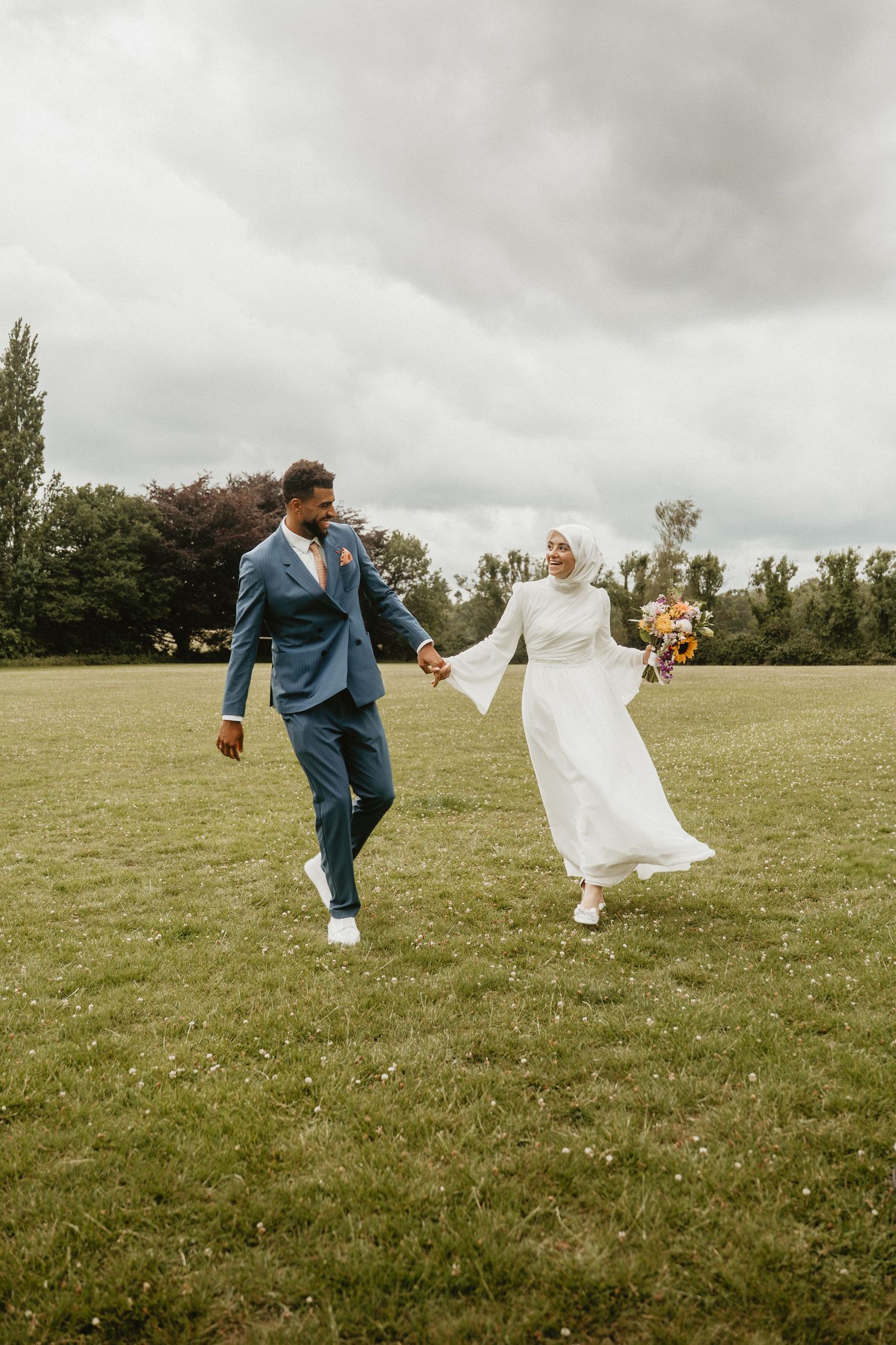 A joyful couple runs and plays in a grassy field during their wedding photoshoot.