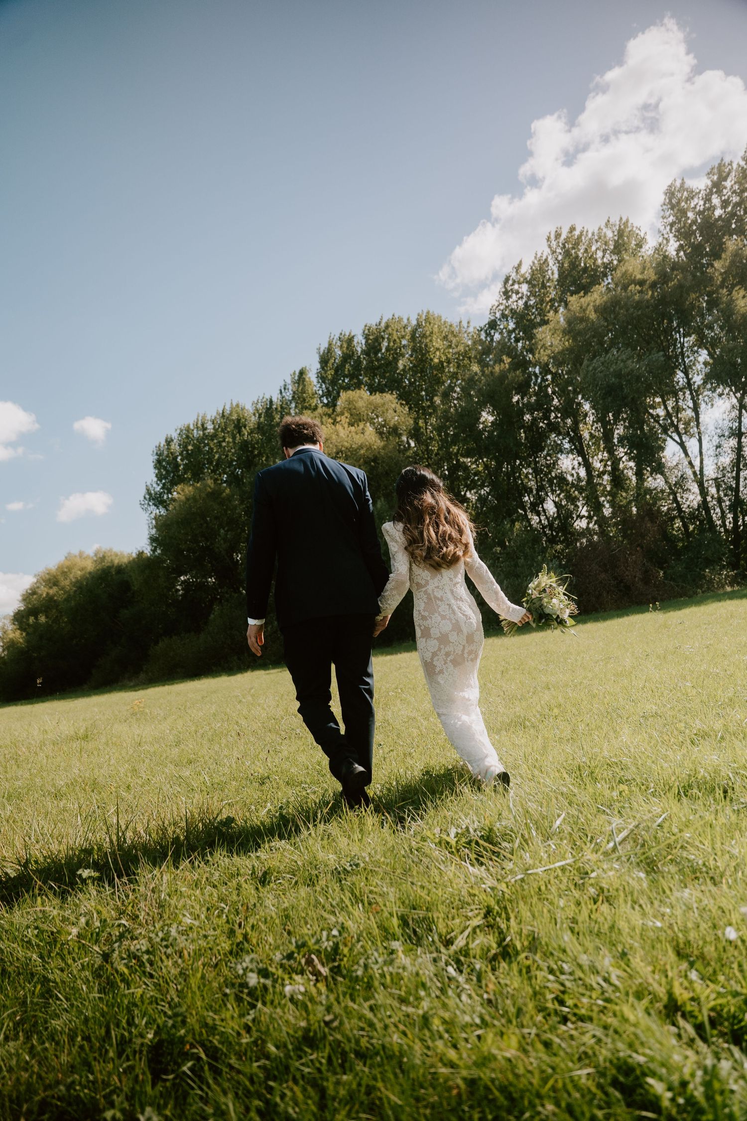 Couple runs playfully through a sunny green field on their wedding day.