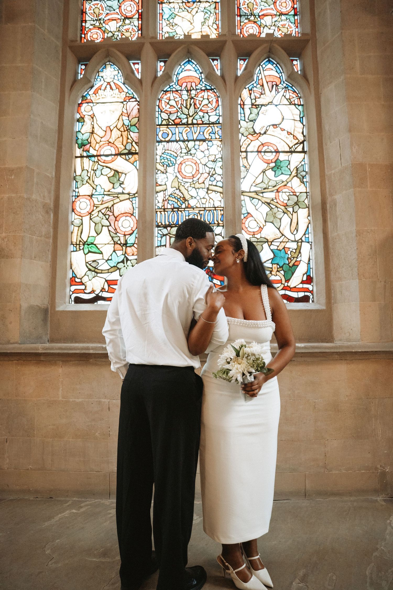 A romantic wedding couple shares intimate moments by stained glass windows in a historic church hallway.