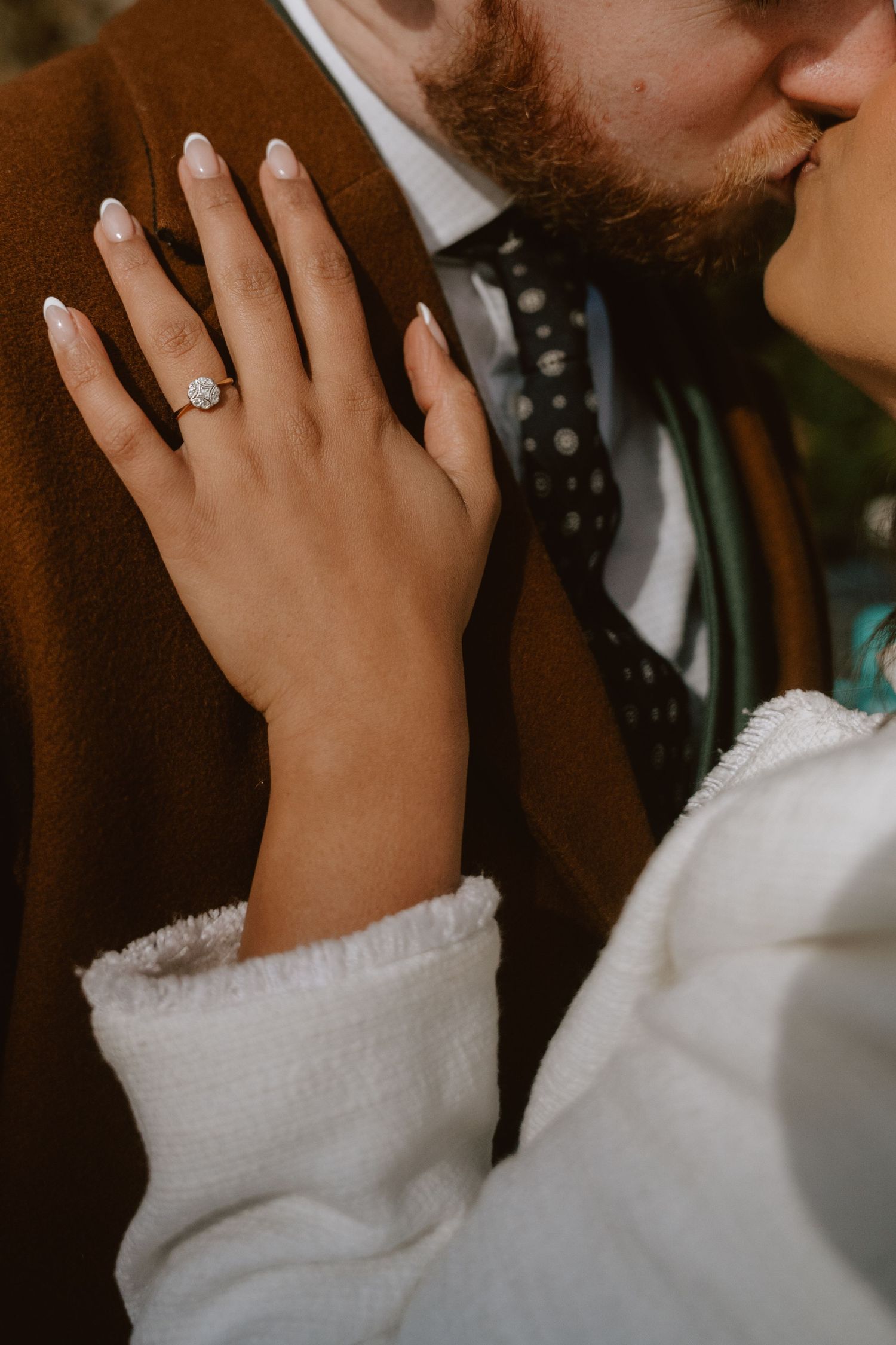 A close-up series of a couple kissing while showing off an engagement ring in a white sweater.