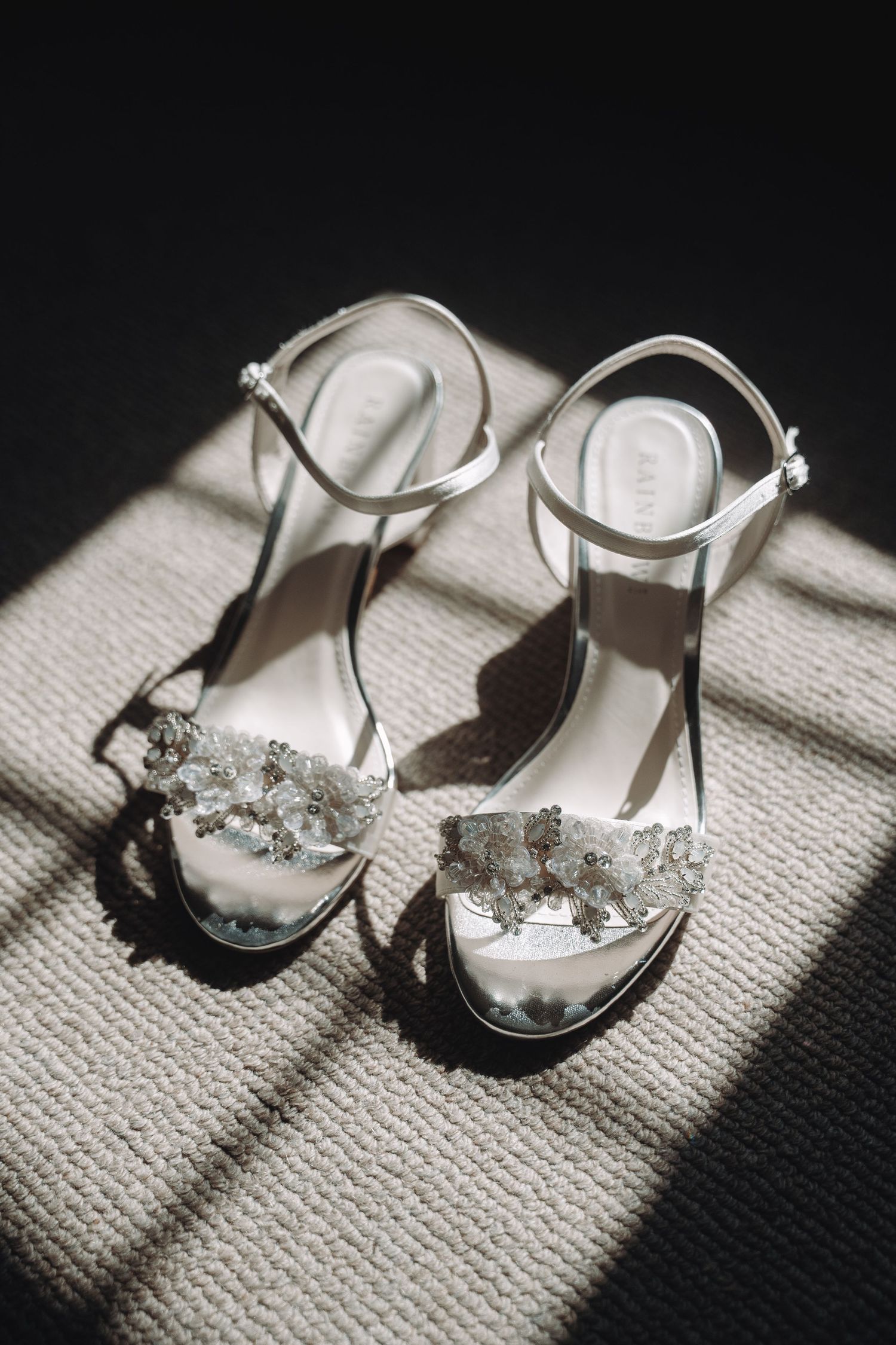 Elegant white bridal shoes with crystal embellishments in dramatic lighting.