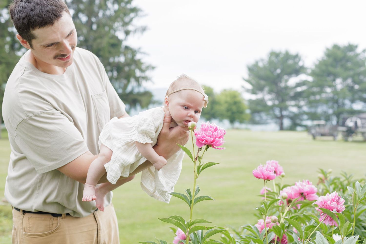 Dad holding newborn daughter over blooming flowers in an outdoor newborn session in Lock Haven Pennsylvania