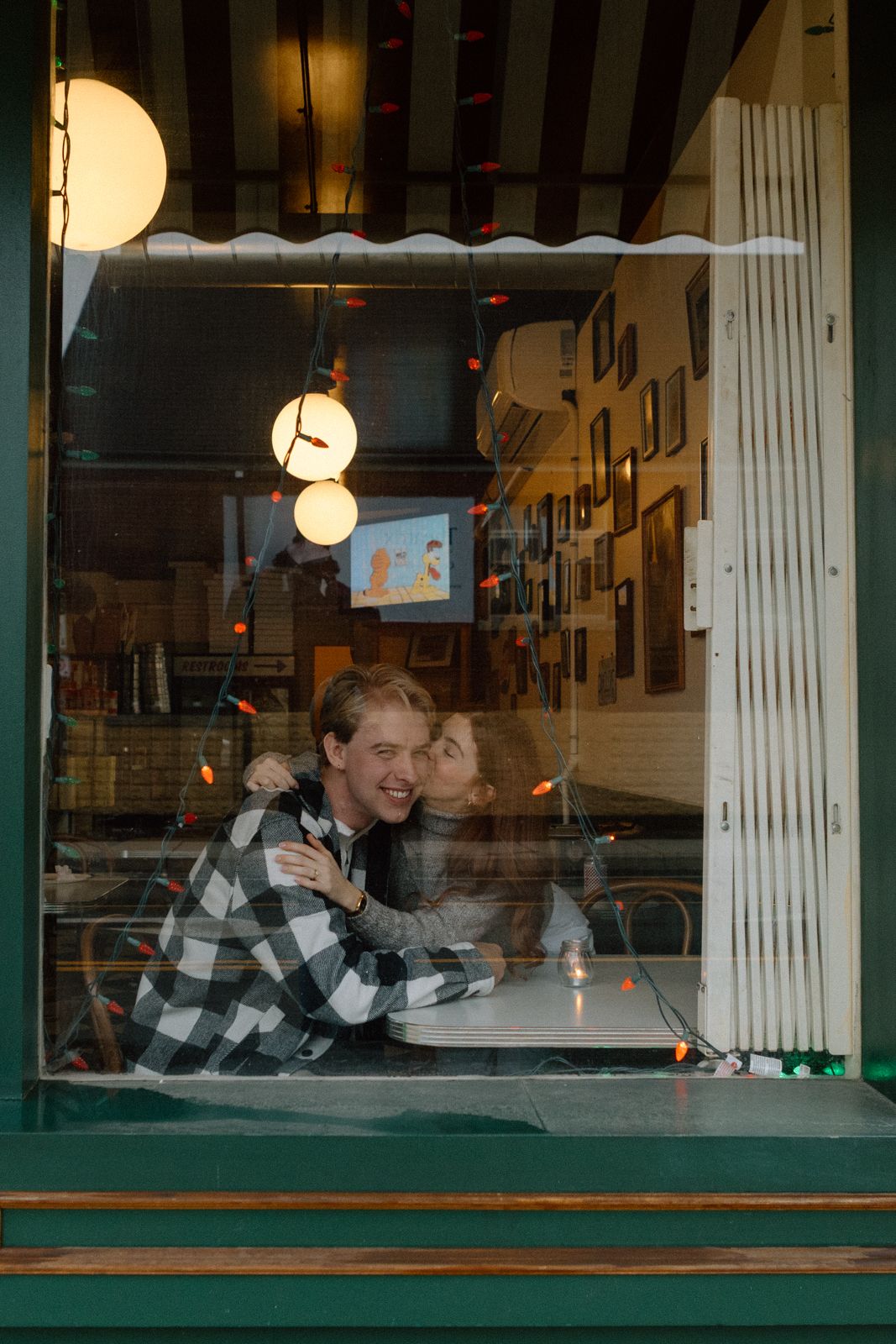 A woman kissing a man in the window of a pizza parlour.