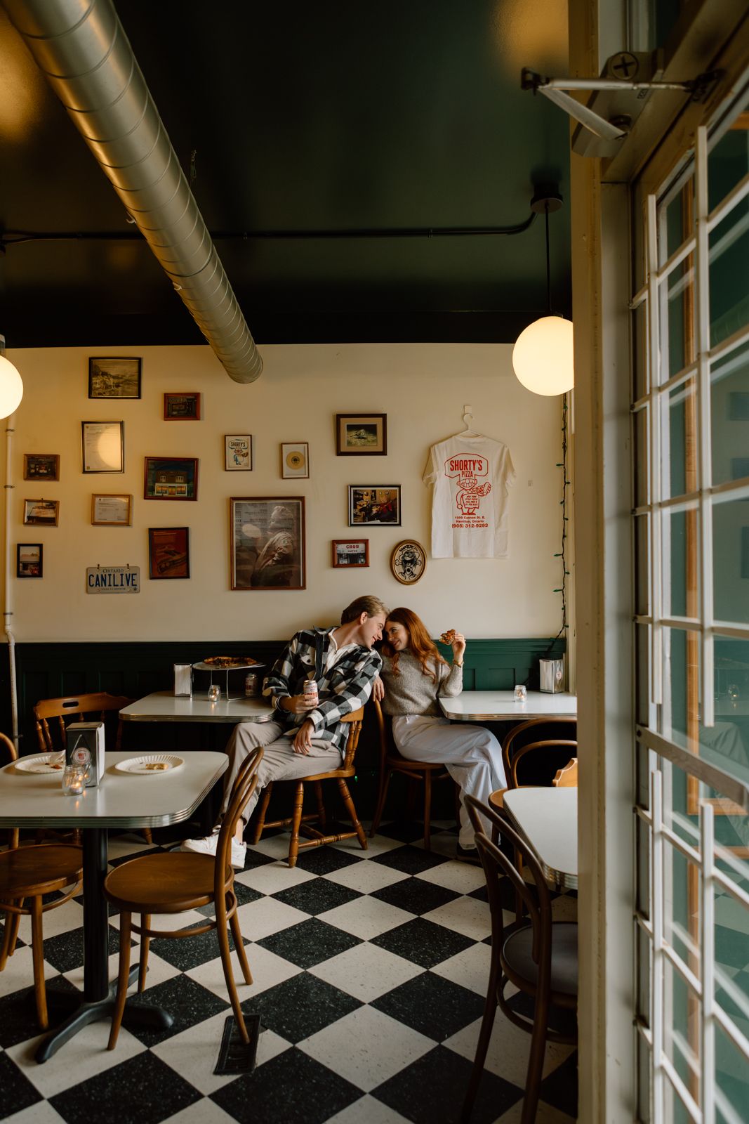 A couple sitting back to back smiling at each other in a pizza parlour.