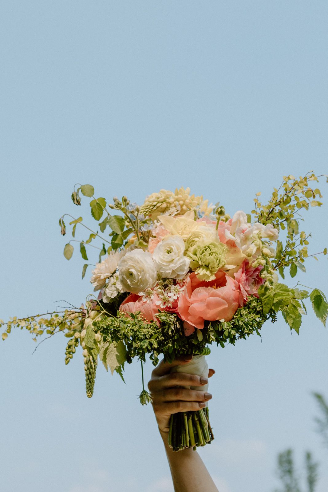 A bride's bouquet, held up against a blue sky.