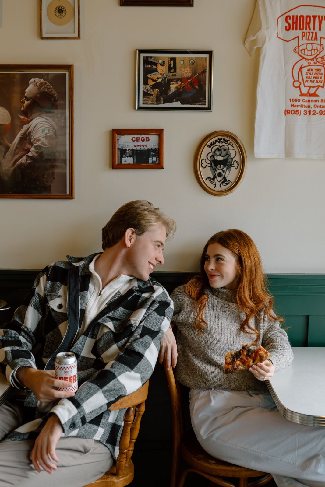 A couple sitting back to back smiling at each other in a pizza parlour.