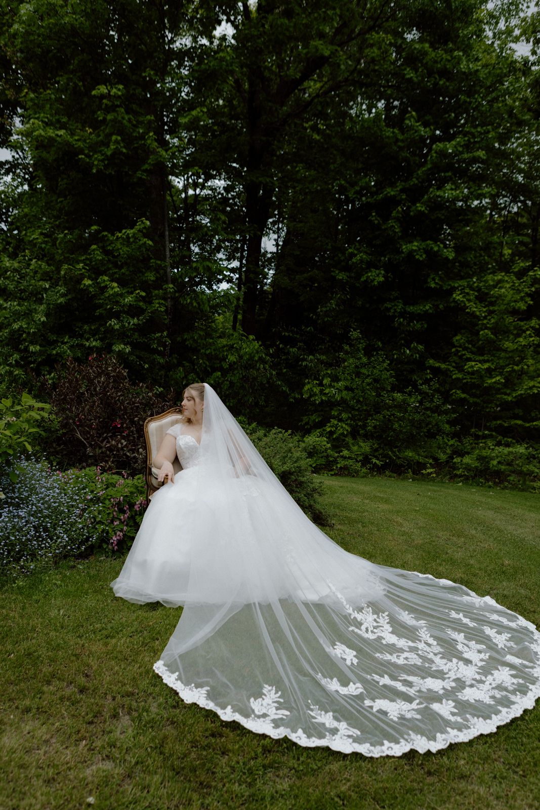 Portrait of a bride sitting in a chair outside on a grassy lawn with a cathedral-length veil.