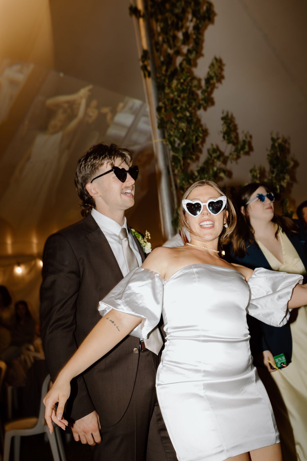 Candid editorial of a bride and groom in their reception clothes and sunglasses on the dance floor at a wedding reception.