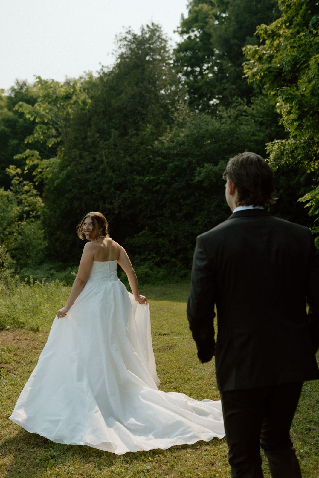 A bride runs into a field smiling over her shoulder at the groom as he runs after her.