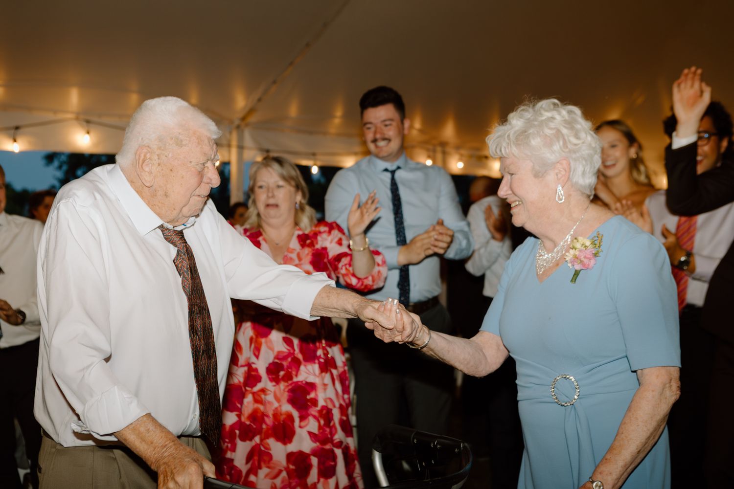 An elderly couple dances together at a wedding reception.