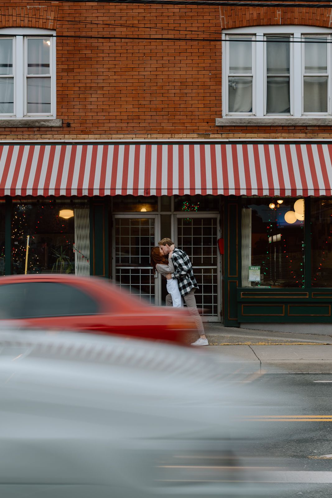 A couple kissing in a busy city street in Hamilton as cars drive past in the foreground.