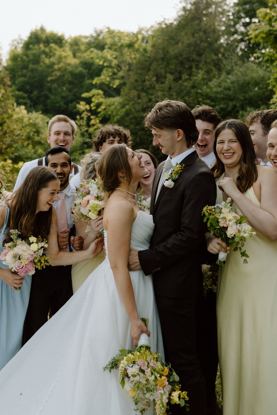 A bride and groom embrace as their wedding party surrounds them.