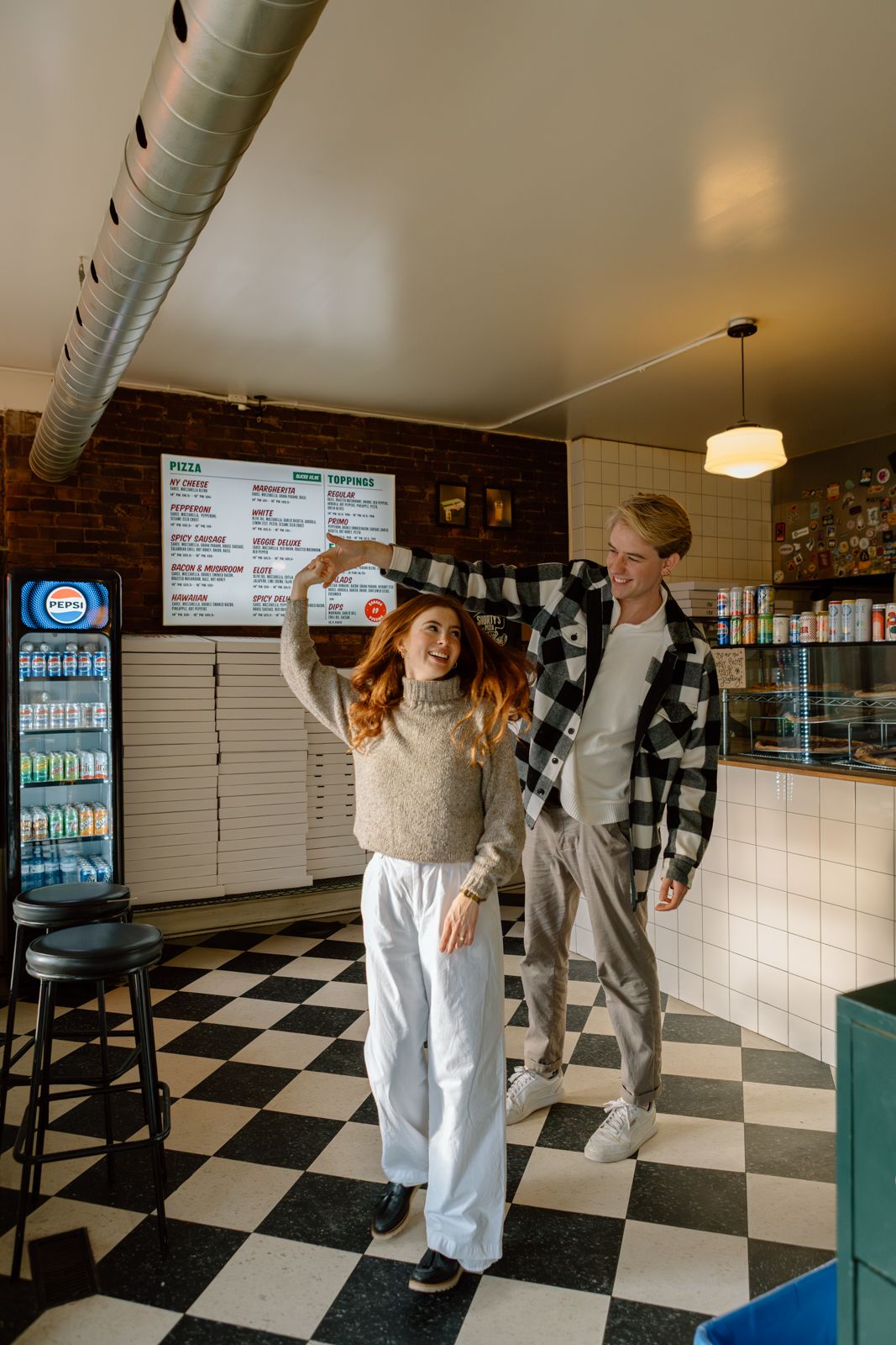 A man and woman dancing in front of the order counter at a pizza parlour.