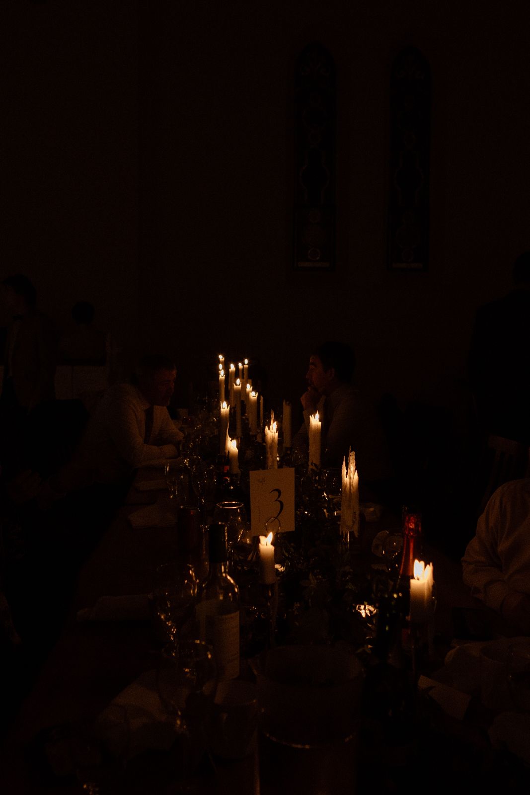 A dark image of candles arranged on a long table at a wedding reception.