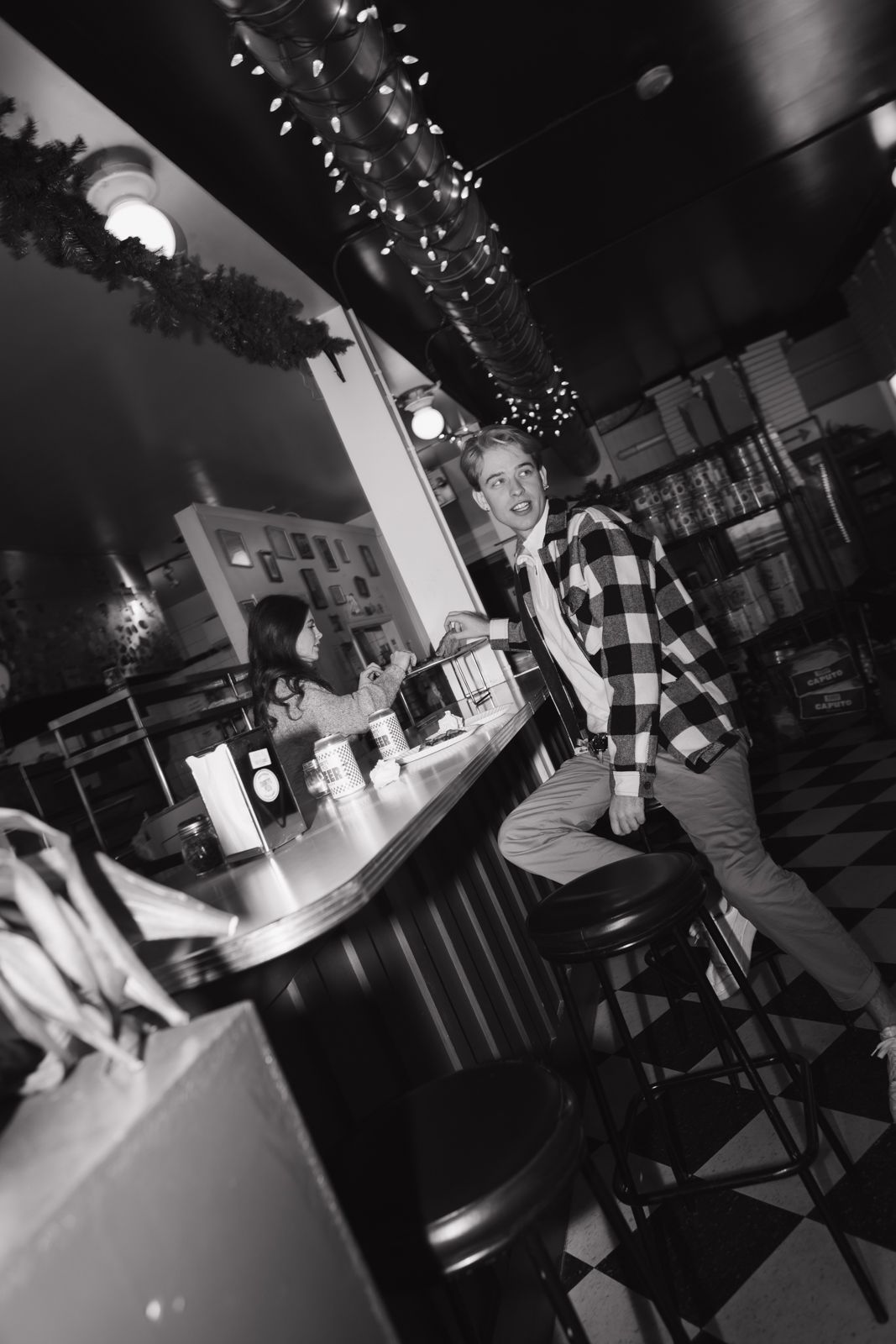 A candid black and white image of a couple sitting at opposite sides of a counter in a pizza parlour.