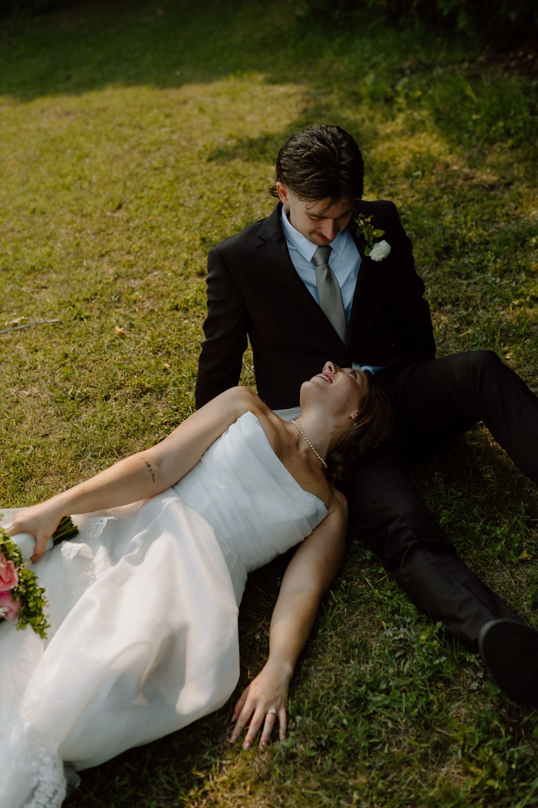 A bride and groom lying in a field looking at each other.
