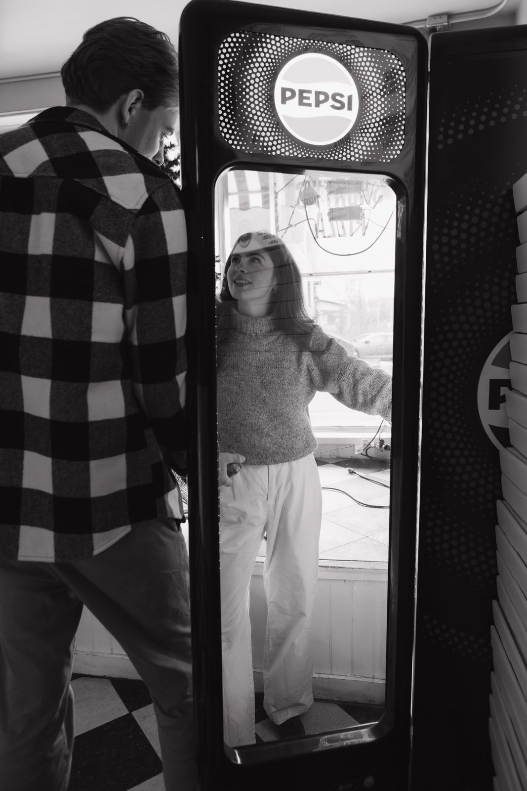 An engaged couple getting drinks out of a pepsi fridge at a pizza parlour.