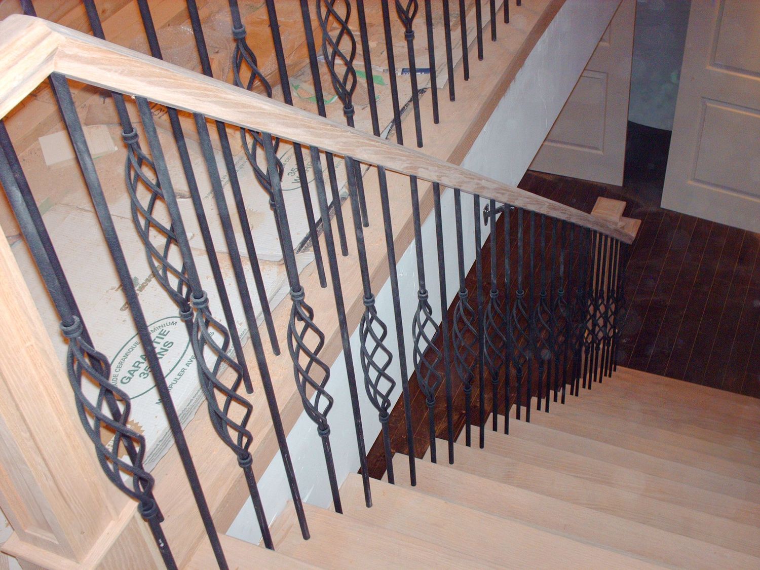 Close-up overhead view of decorative metal basket spindles on oak wood staircase.