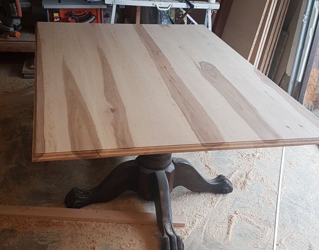 Unfinished natural hickory wood tabletop with visible grain on a dark ornate pedestal base.