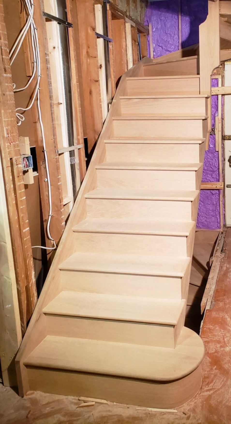 Newly installed unfinished oak staircase with curved bottom step in an under-construction home interior.