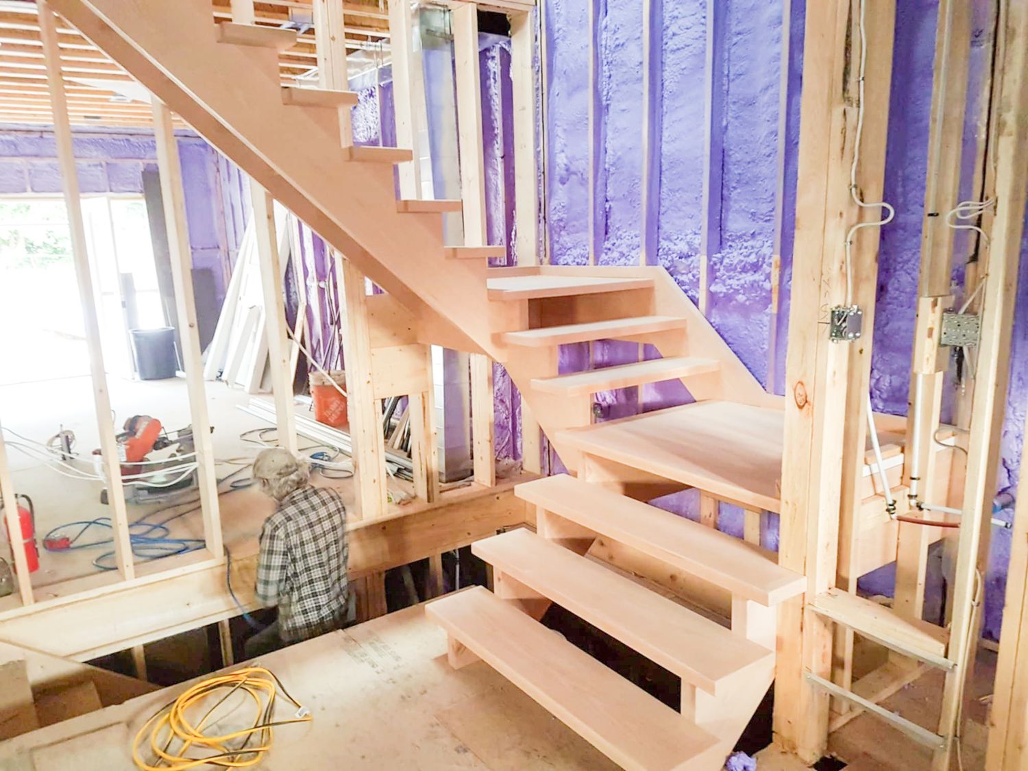 Unfinished floating wood staircase with open risers installed in a home under construction with exposed framing.