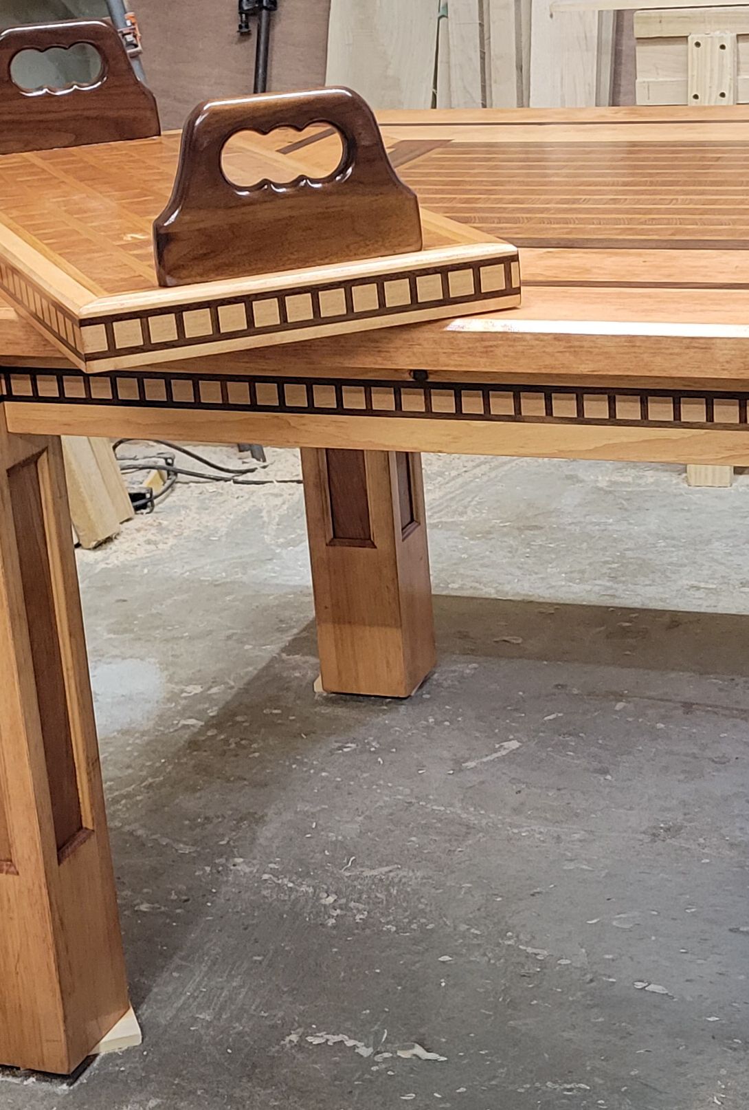 Detail of custom wood dining table corner showing decorative inlay border and matching wooden serving tray.