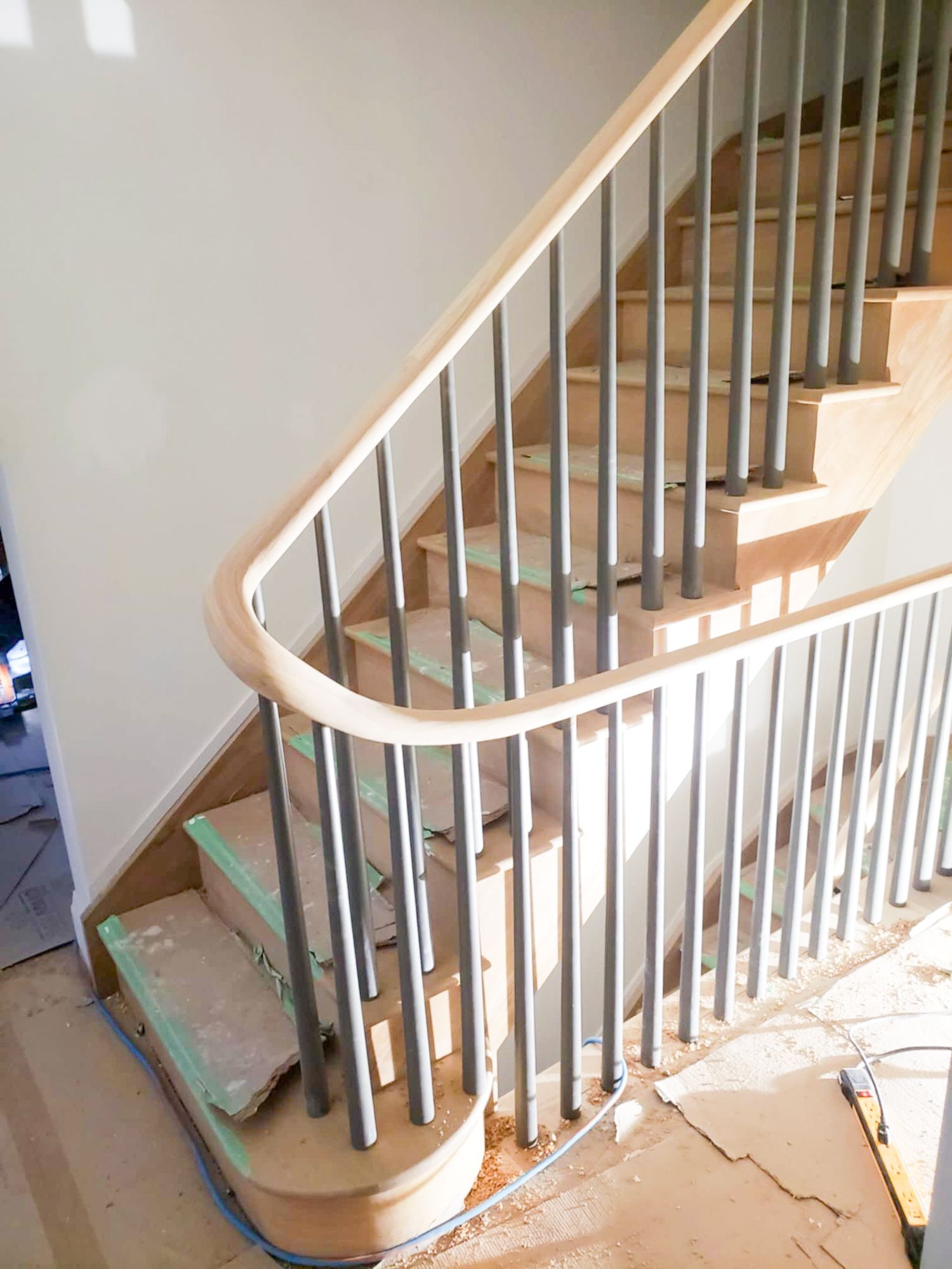 Curved railing on a wooden staircase with sleek wooden spindles and wooden handrail under construction in a residential home.