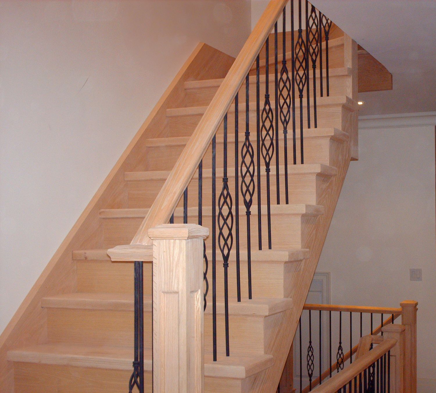 Elegant light oak staircase with black metal pickets and wooden handrail in a residential home.