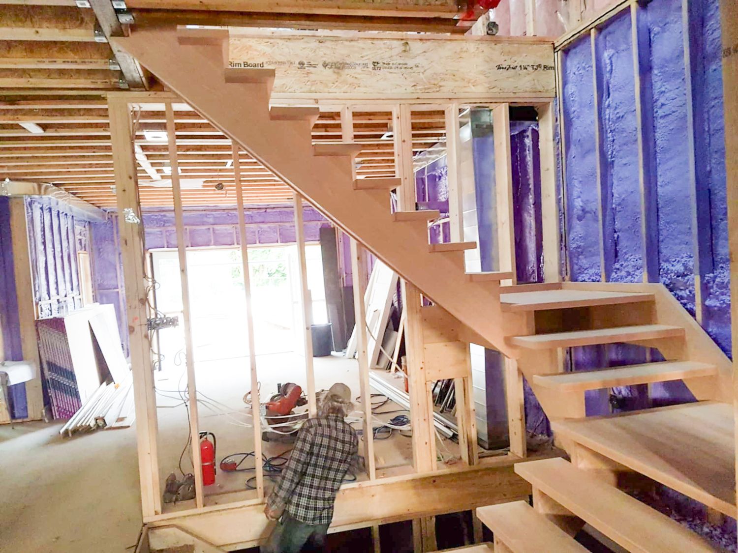 Worker installing open-riser wooden staircase in a home under construction with exposed framing and insulation.