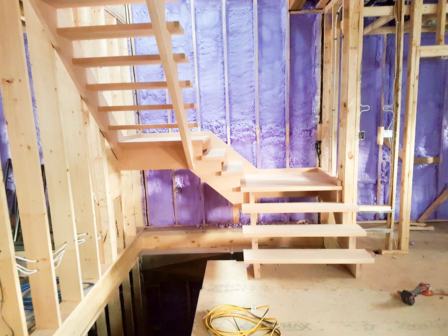 Raw wood open-riser floating staircase under construction in an unfinished framed room with purple insulation.