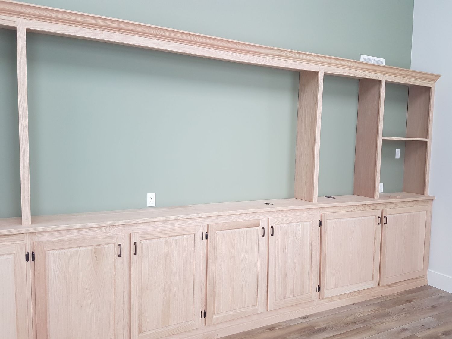 Large unfinished red oak built-in entertainment center with cabinets and shelving.